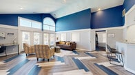 Located at 793 Patriot Pkwy in Rock Hill, South Carolina, this community living room is a thoughtfully designed single-floor gathering space that makes a strong visual impression from the moment you enter. The room's most commanding feature is its soaring vaulted ceiling, which rises dramatically and is adorned with bold cobalt blue paint above a crisp white wainscoting detail — a two-tone design choice that lends the space both energy and elegance.

The flooring is equally eye-catching: a multi-tone herringbone pattern blending warm wood and cool blue-gray planks creates a dynamic, geometric foundation that anchors the entire room. Large floor-to-ceiling windows and glass-paneled French doors flood the space with natural light, while an arched transom window above adds an architectural flourish and draws the eye upward.

The living area is comfortably furnished with a plush sofa, patterned accent chairs, layered rugs, and clustered side tables, creating a welcoming lounge atmosphere. A built-in workstation with granite countertop and seating provides a functional nook for residents. Adjacent to the main seating area, a kitchenette with bar-height seating and a coffee station offers added convenience. The overall ambiance is modern, bright, and community-focused.