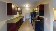 Located at 1829 Furness St in Maplewood, Minnesota, this single-floor unit offers a well-organized layout designed for comfortable, everyday living. The galley-style kitchen is a standout feature, showcasing rich dark wood cabinetry, granite countertops, a stainless steel sink, and a full suite of appliances including a black electric range, stainless steel microwave, and refrigerator. Wood-look flooring runs the length of the kitchen, which also provides access to a dedicated storage closet. The open living area is generously proportioned, finished with plush carpeting, neutral-toned walls, and baseboard heating. A sliding glass door floods the room with natural light and leads directly to a private balcony, offering views of the surrounding area. The bedroom features soft carpeting and a wide sliding-door closet with a full-width hanging rod, providing ample storage. The bathroom is finished with tile flooring, a granite-topped dark wood vanity with an integrated sink, a large mirror, and a full tub-shower combination. Throughout the unit, the consistent use of granite surfaces and dark wood cabinetry creates a cohesive and practical aesthetic, while the neutral color palette lends a clean, move-in-ready feel.