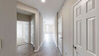 This single-floor, 2-bedroom, 2-bathroom residence offers a thoughtfully designed layout with modern finishes throughout. The open-concept kitchen and living area serves as the heart of the home, featuring white shaker cabinetry, a subway tile backsplash, stainless steel appliances, and a peninsula with an integrated sink — all complemented by light wood-style flooring that flows seamlessly throughout the main areas. The living room benefits from multiple large windows that invite generous natural light, while a striking arched window and vaulted ceiling add an impressive sense of height and openness. A private balcony door extends the living space outdoors. The primary bedroom is a comfortable retreat with vaulted ceilings, plush carpeting, and a large window with outdoor views. Its en-suite bathroom includes a walk-in glass-door shower, a built-in shelving niche, a vanity with stone countertops, and wood-style flooring. The second bedroom also features soft carpeting and ample natural light. The second bathroom offers a full soaking tub and shower combination. A central hallway lined with six-panel doors connects all rooms efficiently, and a dedicated closet provides additional storage. Neutral warm-toned walls and clean white trim unify the space with a bright, cohesive aesthetic.