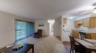 This thoughtfully designed single-floor residence offers a comfortable and functional layout encompassing one bedroom, one bathroom, an office, and a combined living and dining area. The open living room is carpeted and filled with natural light through floor-to-ceiling vertical blinds that lead to a private balcony overlooking a green outdoor space, creating a bright and airy atmosphere. Adjacent to the living area, a dedicated dining space features hardwood-style flooring, providing a clean transition between rooms. The galley-style kitchen is efficiently arranged with warm wood cabinetry, light countertops, a coil-element range, dishwasher, and refrigerator—offering ample storage and workspace. The generously sized primary bedroom features plush carpeting, a large window with vertical blinds for natural light and privacy, and a textured ceiling. A separate office provides a quiet, carpeted workspace complete with a closet for added storage. The full bathroom includes a tiled tub-shower combination, a wood-tone vanity with a light countertop, and tile flooring. Throughout the space, neutral tones, textured ceilings, and consistent finishes create a cohesive and practical living environment well-suited for everyday comfort.