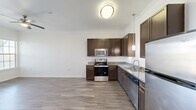 Located in Austin, TX, this thoughtfully designed one-bedroom, one-bathroom residence offers a functional and modern living experience across a single floor. Wood-style flooring runs throughout the entire space, lending warmth and visual continuity from room to room.

The kitchen is a standout feature, equipped with rich dark-brown cabinetry, granite-style countertops, and a full suite of stainless steel appliances including a range, microwave, dishwasher, and refrigerator. Crown molding and pendant lighting add refined finishing touches, while the open layout connects the kitchen seamlessly to the living area, which is outfitted with a ceiling fan.

The bedroom is a comfortable, well-proportioned room featuring a ceiling fan, a window that brings in natural light with views of surrounding greenery, and direct access to a walk-in closet. The closet is generously organized with multiple hanging rods and built-in shelving, offering excellent storage capacity.

The bathroom includes a glass-enclosed walk-in shower, wood-style flooring, granite countertops, and dark cabinetry for additional storage. An in-unit washer is also conveniently accessible within the layout. Clean white walls, crown molding details, and consistent finishes throughout create a cohesive and polished overall ambiance.