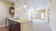 This single-floor, 1-bedroom, 2-bathroom unit offers a thoughtfully designed layout that maximizes functionality and comfort. The open-concept living and kitchen area forms the heart of the home, where a curved granite-topped island with an undermount sink and pendant lighting serves as both a practical workspace and a visual centerpiece. The kitchen is well-equipped with rich dark wood cabinetry, stainless steel appliances including a refrigerator, range, and microwave, and wood-look flooring that adds warmth to the space. The adjoining living area features plush carpeting, a ceiling fan, and multiple windows that invite natural light and outdoor views.

The bedroom is generously sized with soft carpeting, a ceiling fan, and a large window providing natural light. It connects directly to one of the two bathrooms, which features dark wood cabinetry, a granite vanity countertop, and wood-look tile flooring. A walk-in closet with multi-tiered wire shelving systems offers ample storage. The second bathroom provides additional convenience for guests. Throughout the unit, neutral tones, clean lines, and consistent finishes create a cohesive and inviting atmosphere well-suited for comfortable everyday living.