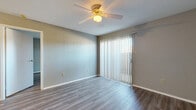 This efficient and thoughtfully laid-out 1-bedroom, 1-bathroom unit is finished with consistent wood-look flooring throughout, lending a cohesive and modern aesthetic to every room. The living area is bright and open, featuring a ceiling fan with light fixture and a sliding glass door dressed with vertical blinds that allows natural light to fill the space and provides access to an outdoor area. The galley-style kitchen is well-equipped with warm wood cabinetry extending to the ceiling for ample storage, light speckled countertops, a double-basin stainless steel sink, a gas range, and a refrigerator — all arranged for an efficient workflow. The bedroom is a comfortable size, also featuring a ceiling fan and a sliding glass door with vertical blinds, offering additional natural light and outdoor views. A dedicated walk-in closet off the bedroom provides generous storage with multiple shelving tiers and hanging rods. The bathroom is outfitted with warm wood cabinetry, a speckled countertop vanity with a large mirror, and a full tub-shower combination with white tile surround. Neutral gray walls and clean white trim are found throughout, creating a simple, move-in-ready environment.