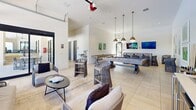 Located at 700 Post Lake Pl in Apopka, Florida, this contemporary community clubhouse spans a single floor and is thoughtfully designed to offer both functional and social spaces. The welcoming lobby greets visitors with soaring ceilings, large-format tile flooring, and floor-to-ceiling glass doors that flood the space with natural light and provide views of the surrounding landscape. Striking gold globe pendant chandeliers hang above a stylish lounge area furnished with leather sofas, accent chairs, and vibrant yellow ottoman accents, complemented by large-scale wall art that adds an artistic focal point. A reception desk anchors the central area, creating a professional yet approachable atmosphere. The game room is a standout feature, equipped with a billiard table, wall-mounted flat-screen televisions, and casual seating arranged beneath warm brass pendant lighting. A dramatic glass garage-style wall opens the space to outdoor views of lush greenery and the pool area, seamlessly blending indoor and outdoor living. Additional areas include a workstation zone with ample desk space and natural light, supporting both productivity and community engagement. Throughout, the consistent use of light tile flooring, crisp white walls, and curated modern furnishings creates a cohesive, upscale ambiance.