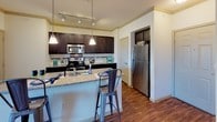 This well-appointed 3-bedroom, 2-bathroom single-story residence offers a thoughtfully designed layout ideal for comfortable everyday living. The main living area welcomes you with rich wood-style flooring, crown molding, and a bright entry door featuring a transom window that fills the space with natural light. A sliding glass door provides additional connectivity to the outdoors.

The kitchen is a standout feature, showcasing dark espresso cabinetry, granite countertops, a mosaic tile backsplash, and stainless steel appliances including a refrigerator and microwave. A peninsula with bar seating and pendant lighting makes the space both functional and inviting, while track lighting adds a modern touch.

Each of the three bedrooms is finished with plush carpet and ceiling fans, and benefits from natural light through well-placed windows with exterior views. The primary bathroom includes a granite-topped vanity, tile flooring, a tub-shower combination, and direct access to a generously sized walk-in closet outfitted with multiple shelving rods and ample storage capacity. The second bathroom mirrors the quality finishes with a granite vanity and a tiled tub-shower combination. Throughout the residence, consistent finishes and a neutral color palette create a cohesive, move-in-ready atmosphere.