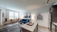 This single-floor residence showcases a thoughtfully designed open-concept layout that seamlessly connects the kitchen, dining, and living areas. The kitchen is a standout feature, boasting sleek dark cabinetry, stainless steel appliances, a subway tile backsplash, track lighting, and a granite-topped island with bar seating — ideal for casual dining or entertaining. The living area flows naturally from the kitchen, offering a warm and inviting atmosphere with light wood-look flooring, neutral walls, and generous natural light from multiple windows. A glass door provides direct outdoor access, further brightening the space.

The bedroom is comfortably scaled, featuring light-filled windows with outdoor views, wood-look flooring, and ample room for a full furniture arrangement. Its clean, neutral palette creates a calm and restful environment. The bathroom includes tile flooring, a tub-shower combination, and straightforward, functional finishes.

Throughout the residence, a consistent modern aesthetic is maintained with neutral tones, clean lines, and well-chosen details. The open flow between living spaces and the abundance of natural light give the home an airy, welcoming feel that is both practical and stylish.