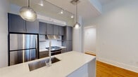 Located at 221 Chartres Street in the heart of New Orleans' historic French Quarter, this 2-bedroom, 2-bathroom unit blends classic character with modern finishes. Warm hardwood floors run throughout, complementing crisp white walls and clean architectural lines. The open kitchen is a standout, featuring slate-gray cabinetry, a herringbone tile backsplash, stainless steel appliances, a gas range, and a white quartz waterfall island with pendant lighting overhead — ideal for both cooking and entertaining. The primary bedroom is a generous retreat highlighted by a dramatic exposed brick wall, high ceilings, and a large window with transom for natural light. The second bedroom offers a bright, clean aesthetic with ample space. Both bathrooms are thoughtfully designed: the primary bath includes a double-sink floating vanity with warm wood cabinetry, large-format tile, and a glass-enclosed walk-in shower, while the secondary bath features subway tile surround, a soaking tub, and a matching wood vanity. Additional highlights include a dedicated closet, ceiling fans, and the timeless charm of a historic New Orleans address just steps from the city's most iconic destinations.