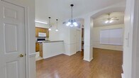 This single-story unit offers two bedrooms and one bathroom within a efficiently designed floor plan. The open living area is distinguished by vaulted ceilings and a ceiling fan, creating a sense of spaciousness beyond its physical footprint. Large windows with blinds allow natural light to fill the room, while arched architectural detailing adds a decorative touch connecting the living and dining spaces. Wood-look flooring runs throughout the main living areas, complemented by tile flooring in the kitchen and bathroom.

The kitchen features warm wood cabinetry, granite countertops, a peninsula with pendant lighting overhead, and white appliances including a refrigerator, stove, and built-in microwave. A stainless steel sink is set into the granite surface, and tile flooring completes the space.

The primary bedroom is a comfortable size, with wood-look flooring and access to the hallway. The second bedroom is more compact but equally well-finished. Both rooms feature neutral white walls and panel-style doors.

The bathroom includes a granite-topped vanity with wood cabinetry, a mirrored medicine cabinet, a tub-shower combination with white tile surround, and tile flooring. A hallway connects all rooms efficiently throughout the unit.
