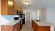 Located at 2980 Mark Andrew Dr in Columbus, Ohio, this single-floor residence offers a well-designed layout with a cohesive blend of wood-tone finishes and neutral color palettes throughout. The kitchen is a central highlight, featuring rich warm-toned cabinetry, granite-style countertops, a peninsula with an undermount sink, and a full suite of black appliances including an electric range, over-the-range microwave, and refrigerator. Wood-look vinyl plank flooring runs through the kitchen and main living areas, creating a clean, durable foundation. The open-concept kitchen flows seamlessly into the living space, which transitions to plush carpeting for added comfort. A long hallway connects the main living areas to the private spaces of the home, maintaining a clear and organized flow. The residence includes two bathrooms: one featuring a shower-tub combo with a curved rod and a warm wood vanity, and a second en-suite style bathroom with a standalone glass-enclosed shower stall and matching vanity. Bedrooms are carpeted and offer generous proportions with neutral walls. A dedicated in-unit laundry area houses a full-size washer and dryer, adding everyday convenience. The space presents a practical and comfortable living environment suitable for a variety of lifestyles.