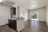Located at 268 E James Court Dr in Meridian, Idaho, this single-floor residence offers a well-designed, open-concept layout that maximizes both functionality and comfort. The kitchen is a standout feature, equipped with rich dark-espresso cabinetry, light countertops, black appliances including a refrigerator and range, and a peninsula with a double sink that opens directly into the living area. Light wood-style flooring runs throughout the kitchen and living spaces, lending a clean, cohesive aesthetic. The living room is bright and inviting, benefiting from natural light that pours in through a large sliding glass door leading to a private balcony with outdoor views of mature trees and the surrounding community. The bedrooms are carpeted for added comfort, with multiple windows fitted with blinds that allow for natural light control. One bedroom features dual windows offering views of the landscaped surroundings. The bathroom includes dark cabinetry, a vanity, and a walk-in shower enclosed with a frosted glass door, finished with wood-style flooring. Textured ceilings are present throughout the residence, adding subtle architectural character. Overall, the space presents a clean, neutral palette ideal for a variety of living arrangements.