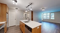This single-floor residence offers a thoughtfully designed layout encompassing two bedrooms, two bathrooms, a combined kitchen and living area, and a dedicated closet. The open-plan kitchen is a standout feature, showcasing warm wood cabinetry, a white subway tile backsplash, stainless steel appliances, and a curved central island with a white countertop and pendant lighting — ideal for both cooking and casual dining. The living area flows naturally from the kitchen and is finished with rich, dark hardwood-style flooring, with large windows and a glass door that invite abundant natural light and frame views of the surrounding greenery.

The primary bedroom is a comfortable, well-proportioned retreat featuring plush carpeting, corner windows with views of mature trees, and a ceiling fan with integrated lighting. The second bedroom also features soft carpeting, a large window overlooking the outdoors, and a sliding door closet for convenient storage. Both bathrooms are finished with warm wood vanities, white countertops, and durable hardwood-style flooring; one includes a shower-tub combination. Neutral tones and consistent finishes throughout the space create a cohesive and inviting atmosphere.
