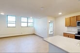 This single-floor residence offers a thoughtfully designed layout encompassing two bedrooms, two bathrooms, a kitchen, a living room, and a closet. The open-concept kitchen is outfitted with warm honey-toned wood cabinetry, stainless steel appliances including a refrigerator, range, and microwave, light-colored countertops, and a central island with a built-in sink — providing ample workspace and storage. The kitchen flows naturally into the living area, which features light tile flooring, recessed lighting, and a row of windows that invite natural light and offer pleasant outdoor views of surrounding greenery. The bedrooms are carpeted for comfort, with the primary bedroom offering generous proportions and dual doorways providing convenient access. The second bedroom also benefits from natural light through a window with outdoor views. Both bathrooms are cleanly finished with tile flooring, warm wood vanities, white countertops, and walk-in shower stalls equipped with grab bars, reflecting a practical and accessible design. Throughout the residence, neutral white walls and recessed lighting create a clean, bright ambiance. The consistent use of light tones and functional finishes gives the space a cohesive and move-in-ready character.