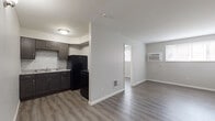 Located at 257 S. Central Ave. in Columbus, Ohio, this single-floor unit offers a clean, updated interior with a consistent modern aesthetic throughout. The layout connects the kitchen and living area in an open, functional arrangement, with a partial dividing wall separating the two spaces while maintaining an airy feel. Natural light enters through windows fitted with blinds, complementing the neutral gray walls and light wood-look vinyl plank flooring found throughout the unit.

The kitchen is well-appointed with dark espresso-toned shaker-style cabinetry, light granite-look countertops, and a textured stone tile backsplash. Black appliances, including a refrigerator and range, provide a cohesive look, and a range hood is installed above the cooking area. The sink is positioned centrally along the lower cabinetry, offering ample counter space on either side.

The living area is spacious and versatile, featuring a wall-mounted air conditioning unit and a floor vent for heating. A separate bedroom provides a quiet retreat with its own window allowing natural light. The bathroom includes a full-size soaking tub with a clean white surround. The overall design is straightforward and practical, maintaining a fresh, move-in-ready condition throughout.