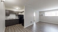 Located at 257 S. Central Ave. in Columbus, Ohio, this single-floor unit offers a clean, updated interior with a consistent modern aesthetic throughout. The layout connects the kitchen and living area in an open, functional arrangement, with a partial dividing wall separating the two spaces while maintaining an airy feel. Natural light enters through windows fitted with blinds, complementing the neutral gray walls and light wood-look vinyl plank flooring found throughout the unit.

The kitchen is well-appointed with dark espresso-toned shaker-style cabinetry, light granite-look countertops, and a textured stone tile backsplash. Black appliances, including a refrigerator and range, provide a cohesive look, and a range hood is installed above the cooking area. The sink is positioned centrally along the lower cabinetry, offering ample counter space on either side.

The living area is spacious and versatile, featuring a wall-mounted air conditioning unit and a floor vent for heating. A separate bedroom provides a quiet retreat with its own window allowing natural light. The bathroom includes a full-size soaking tub with a clean white surround. The overall design is straightforward and practical, maintaining a fresh, move-in-ready condition throughout.