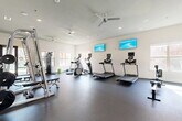 Located at 1633 Greenridge Drive in Burleson, TX, this single-floor fitness center offers a generously sized, open workout environment designed to accommodate a full range of exercise disciplines. The space features durable rubber flooring throughout, crisp white walls, and recessed lighting complemented by ceiling fans that maintain a comfortable atmosphere during workouts.

The cardio zone is equipped with multiple treadmills and elliptical machines, each fitted with individual display screens, and wall-mounted flat-screen TVs provide additional entertainment. A dedicated strength training area houses a multi-station cable machine, a smith machine with bench press setup, and a full rack of dumbbells arranged along a mirrored wall, allowing users to monitor their form with ease.

A separate functional training area features a freestanding punching bag, a wall-mounted display, and a dumbbell rack, bathed in natural light from arched windows that frame views of the surrounding greenery. An adjacent room provides additional space and connects to a restroom facility. Large glass doors open directly to the outdoor area, enhancing the sense of openness and providing convenient access to exterior amenities. The overall design is clean, modern, and highly functional, making this fitness center a comprehensive resource for residents.