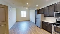 This single-story residence offers a clean, functional layout designed to maximize everyday comfort. The open living area is finished with warm wood-style laminate flooring that extends throughout, creating a cohesive and easy-to-maintain surface underfoot. Recessed lighting and a ceiling fan with light fixture provide ample illumination and air circulation, while a window along the exterior wall invites natural light into the space.

The kitchen sits adjacent to the living area in an open-concept arrangement, featuring rich dark espresso-toned cabinetry both above and below the countertop. Light-colored counters provide a contrasting work surface, complemented by a white subway tile backsplash. A full-size stainless steel refrigerator anchors the kitchen, and the cabinetry offers generous storage for everyday essentials.

The neutral wall tones throughout the space lend a versatile backdrop that accommodates a variety of interior styles. The overall layout is straightforward and efficient, making it well-suited for those seeking a manageable, low-maintenance living environment on a single level.