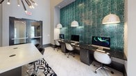 Located at 15250 Siesta Key Way in Rockville, Maryland, this single-floor amenity space is designed with a sophisticated, contemporary aesthetic that blends functionality with upscale design. The space is anchored by a striking business center featuring a long dark granite-topped workstation set against a dramatic textured teal accent wall. Multiple iMac workstations are illuminated by globe pendant lights, while large floor-to-ceiling windows flood the area with natural light and provide views to the exterior. Polished marble-look tile flooring runs throughout, contributing to the clean, modern atmosphere.

A glass-enclosed conference room offers a refined meeting environment, accessible through sliding glass doors etched with decorative motifs. Inside, a sleek conference table is surrounded by upholstered chairs beneath an artistic chandelier, with a display screen positioned for presentations.

The lounge area impresses with soaring double-height ceilings, dramatic pendant lighting, and thoughtfully curated furnishings including tufted navy blue wall panels, contemporary seating, and decorative wall art. A built-in media cabinet with a wall-mounted television serves as a focal point. Additional seating areas with bistro-style tables offer casual gathering spots. Large glass doors connect the lounge directly to an outdoor area, enhancing the sense of openness and flow throughout the space.