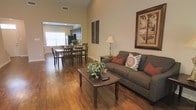 Located at 8254 County Road 64 in Daphne, Alabama, this two-story home offers a well-designed layout that balances comfort and functionality. The main living area immediately impresses with its soaring vaulted ceilings that amplify the sense of openness and space. Rich hardwood flooring flows throughout, lending warmth and continuity to the interior.

The living room serves as a welcoming central hub, featuring ample space for seating and accented by large framed wall art and tasteful décor. Natural light filters in through generously sized windows, brightening the space throughout the day. The open-concept design connects the living room seamlessly to the dining area, which comfortably accommodates a full dining set — ideal for both everyday meals and entertaining.

Just beyond the dining space, the kitchen is visible and accessible, offering a practical flow between cooking and gathering areas. The neutral wall tones throughout complement the warm flooring and create a cohesive, inviting atmosphere.

Spanning two floors, the home provides a clear separation between the communal living spaces on the main level and additional rooms above, offering both privacy and versatility. The overall design reflects a traditional yet functional aesthetic well-suited to the Daphne, Alabama community.