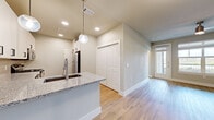 This thoughtfully designed single-floor residence offers a cohesive open-concept layout finished with light hardwood flooring that runs seamlessly throughout every room. The entrance features a built-in mudroom with white open shelving and hooks, providing organized storage from the moment you step inside. A hallway connects the main living areas, leading to the kitchen and beyond.

The kitchen is outfitted with white shaker cabinetry, granite countertops, a subway tile backsplash, and a full suite of stainless steel appliances including a gas range, microwave, dishwasher, and refrigerator. A peninsula with an undermount sink and pendant lighting overhead adds both function and style, opening naturally toward the living area. A large closet with double doors sits just off the main living space for additional storage.

The bedroom is a comfortably sized retreat featuring a ceiling fan, a wide window that draws in natural light and offers outdoor views, and direct access to a walk-in closet equipped with wire shelving systems along multiple walls. The bathroom includes white cabinetry, granite countertops, and a soaking tub with marble-style tile surround. Soft neutral tones and clean white trim throughout give the entire space a bright, modern, and move-in-ready feel.