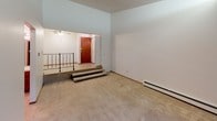 Located at 9106 W Lisbon Ave in Milwaukee, Wisconsin, this single-floor unit offers a thoughtfully arranged layout with a distinctive split-level entryway. Upon entry, a set of steps leads up to the main living area, which is anchored by soaring ceilings and carpeted flooring throughout. A ceiling fan and baseboard heating ensure year-round comfort, while a large sliding glass door floods the space with natural light and provides views of surrounding greenery — complemented by built-in shelving along the adjacent wall.

The galley-style kitchen is well-equipped with warm wood cabinetry lining both walls, generous counter space, a double-basin sink, a gas range, and a full-size refrigerator. A closeted pantry area provides additional storage. The tile flooring adds a practical, easy-to-maintain surface to the space.

The bathroom features mosaic tile flooring, a full tub and shower surround with integrated shelving, and a toilet, all accessed through a classic wood-framed door. A separate vanity area offers a wide wood cabinet base, double-door storage, an extended countertop with a single sink, and a large lighted mirror — ideal for daily routines. Additional carpeted rooms provide flexible living or sleeping spaces, each finished with neutral walls and baseboard heating.