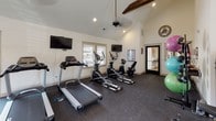 Located at 1862 Brevard Rd in Arden, NC, this single-story fitness center is designed to support a full range of workout routines in a welcoming, functional environment. The space is defined by vaulted ceilings with an exposed wooden beam that adds a rustic architectural touch, complemented by ceiling fans that help maintain comfortable airflow throughout. A bold orange accent wall energizes the atmosphere and visually divides the space into distinct workout zones.

The flooring throughout is durable rubber matting, ideal for heavy equipment and high-impact exercise. The cardio area features multiple treadmills, elliptical machines, and a recumbent bike, all positioned facing wall-mounted televisions and windows fitted with blinds that allow natural light while maintaining privacy. A large mirror runs along one wall of the strength-training area, enhancing the sense of space and allowing users to monitor their form.

The strength zone is comprehensively outfitted with cable machines, a multi-station weight machine, free weights on a dedicated rack, adjustable benches, and a leg press. Additional accessories such as stability balls and resistance equipment are neatly stored in a dedicated corner. Direct exterior access via a glass-paned door connects the space to the surrounding outdoor grounds.