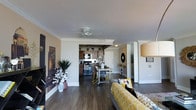 This single-floor unit at 800 City Tower Apartments showcases an open-concept design that connects the living, dining, and kitchen areas into one cohesive, functional space. Dark hardwood floors run throughout, providing a rich, grounding contrast to the neutral-toned walls and white crown molding that frames the ceilings with a clean, polished finish.

The living area is bright and welcoming, accented by a ceiling fan that adds both practicality and visual interest. A large cityscape wall mural serves as a bold focal point, complementing the urban setting of the building. Lush potted plants add natural warmth and vibrancy to the space.

The dining area transitions naturally from the living space and features a compact yet stylish table arrangement, ideal for everyday meals or casual entertaining. Just beyond, the kitchen is equipped with dark wood cabinetry, stainless steel appliances including a range and microwave, and ample counter space for meal preparation.

The overall ambiance is modern and urban, blending practical design with decorative touches that make the space feel lively and curated. The open layout maximizes the sense of space, making the unit feel expansive and airy throughout.