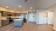 This single-floor residence offers a thoughtfully designed open-concept layout that seamlessly connects the kitchen and living areas. The kitchen is a functional centerpiece, featuring warm taupe shaker-style cabinetry, light quartz countertops, stainless steel appliances including a refrigerator, gas range, microwave, and dishwasher, and a central island that provides additional prep space and storage. Wood-look luxury vinyl plank flooring extends throughout the main living areas, lending a clean, contemporary feel.

The spacious living room benefits from large windows fitted with horizontal blinds, a ceiling fan, and a private exterior door, filling the space with natural light and offering outdoor access. The bedrooms are carpeted for comfort and each includes generous closet space, with at least one bedroom featuring a dedicated walk-in closet. A conveniently located in-unit laundry area is accessible from the bedroom hallway.

The primary bathroom is appointed with a dual-sink vanity, taupe cabinetry, and a walk-in shower, while the secondary bathroom features a full tub-shower combination with subway tile surround. Neutral wall tones and recessed lighting throughout create a cohesive, move-in-ready ambiance suited for modern living.