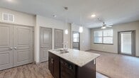 This thoughtfully designed 1-bedroom, 1-bathroom residence offers a functional and modern single-floor layout. The open-concept kitchen serves as the heart of the home, featuring dark espresso cabinetry, granite countertops, black appliances including an electric range and built-in microwave, and a central island with a stainless steel sink and pendant lighting above. Wood-style flooring runs throughout the kitchen and main living areas, creating a seamless and cohesive aesthetic.

The living room is bright and comfortable, with a ceiling fan, natural light from large windows with blinds, and plush carpet flooring. The bedroom is a well-sized retreat, also carpeted and ceiling fan-equipped, with a large window offering outside views. It provides direct access to the full bathroom, which features granite countertops, a dark vanity, wood-style flooring, and an adjacent walk-in closet outfitted with wire shelving systems for ample organization.

Additional highlights include two closets, two pantry spaces, a dedicated laundry area, and a utility room, providing exceptional storage throughout. The overall palette of neutral tones, gray-paneled doors, and consistent finishes lends the space a clean, modern character.