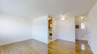 This single-floor residence offers a clean, functional layout designed for comfortable everyday living. The main living area is bright and open, showcasing polished hardwood floors that reflect natural light and lend warmth to the space. Crisp white walls provide a neutral backdrop, while a ceiling fan overhead adds both practical ventilation and a subtle decorative touch.

Adjacent to the living area, the kitchen is partially separated by a dividing wall, creating a sense of distinction between spaces while maintaining an open feel. The kitchen features warm-toned wood cabinetry that adds character and storage functionality, complemented by white appliances including a gas range and an overhead microwave. The light-colored flooring in the kitchen coordinates seamlessly with the rest of the home.

The overall layout is straightforward and efficient, making excellent use of the available floor plan. The consistent use of light tones throughout — from the walls and ceilings to the floors — creates a cohesive and airy ambiance. The space is well-suited for those seeking a tidy, move-in ready home with classic finishes and a practical design that balances openness with defined functional zones.
