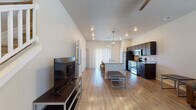 This two-story space is designed with a functional, modern layout that distributes living areas across both floors. The main level opens into a spacious, open-concept living and kitchen area finished with light wood-look flooring and recessed lighting. The kitchen is well-appointed with dark espresso cabinetry, stainless steel appliances including a refrigerator, range, and microwave, and granite countertops that extend to a peninsula with bar seating. Industrial-style pendant lights hang above the peninsula, adding a contemporary touch. The living area accommodates comfortable seating and connects seamlessly to the rest of the main floor.

A secondary living or flex space is also present, featuring light wood flooring, large windows with blinds, and ample natural light. The bedrooms, located on the upper level, are carpeted and include ceiling fans, dual windows with blinds, and dedicated desk areas suitable for study or work. The bathrooms feature dark vanity cabinetry with granite countertops, undermount sinks, lighted mirrors, and tub-shower combinations with tile surrounds and wood-look flooring. A staircase connects both levels, completing this well-organized, multi-room layout.