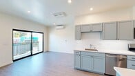 Located at 201 River Street in Santa Cruz, California, this efficiently designed single-floor unit offers a thoughtfully laid-out living space. The open-concept living area is bright and airy, featuring light-toned hardwood-style flooring, recessed lighting, and crisp white walls that create a clean, modern aesthetic. A wall-mounted mini-split HVAC unit ensures year-round comfort. Large sliding glass doors lead directly to a private balcony, flooding the interior with natural light and offering open views of the surrounding Santa Cruz streetscape, palm trees, and blue California skies. The galley-style kitchen is well-appointed with sage-toned shaker cabinetry, white quartz countertops, and a full suite of stainless steel appliances including a gas range, microwave, dishwasher, and refrigerator. A secondary kitchenette area with additional cabinetry and a sink is visible in the main living space, adding extra functionality. The unit also includes a dedicated entrance, a closet for storage, and a full bathroom. The overall ambiance is clean, contemporary, and move-in ready, reflecting modern construction finishes throughout. Its River Street address places it within easy reach of downtown Santa Cruz amenities.