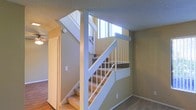 This two-story residence offers a thoughtfully arranged layout spread across two levels, connected by a carpeted staircase framed with crisp white wood railings and balusters. The staircase serves as a central architectural element, with windows positioned along the stairwell that allow natural light to filter in and brighten the transitional space between floors. The warm, neutral-toned walls in a soft beige palette create a welcoming and cohesive atmosphere throughout. On the lower level, hardwood flooring adds a touch of warmth and character to the living areas, while plush carpeting in the stairway and upper portions of the home provides comfort underfoot. A ceiling fan is visible in an adjoining room, contributing to the home's practical and functional design. The textured ceilings and clean white trim work complement the overall aesthetic, lending a classic residential feel. The open sightlines and natural illumination from the stairwell windows enhance the sense of spaciousness within the home, making it feel bright and airy. Overall, the space presents a comfortable, well-lit two-level home with a traditional design sensibility and inviting interior finishes.