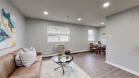 This well-appointed single-floor residence offers a cohesive and modern living experience through its clean design and updated finishes throughout. The open-concept living and dining area is anchored by cool-toned gray walls, recessed lighting, and durable wood-look flooring that extends seamlessly across the space. Natural light filters in through multiple windows fitted with blinds, creating a bright and airy atmosphere. The living area provides a comfortable, functional layout with ample room for seating and entertaining, while a dedicated dining nook adds practical separation within the open plan.

The kitchen is efficiently designed in an L-shaped configuration, showcasing crisp white shaker cabinetry with matte black hardware, a striking turquoise subway tile backsplash, and a full suite of stainless steel appliances including a range, over-the-range microwave, and a full-size refrigerator. Light countertops and a modern sink complete this well-equipped culinary space.

The two bedrooms feature soft carpeting, gray walls, and windows offering garden views, providing a calm and restful environment. The bathroom is a standout, featuring bold turquoise subway tile lining the walls of a full soaking tub surround, complemented by a window that brings in natural light. Throughout the unit, baseboard heating and consistent neutral tones contribute to a practical yet stylish overall aesthetic.