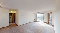 This single-floor residence offers a functional and comfortable layout across several well-defined spaces. The living room is generously proportioned, featuring neutral carpet, white walls, and a sliding glass door that opens to a private balcony with outdoor views of surrounding greenery, allowing abundant natural light to fill the room. A ceiling fan with a light fixture is positioned near the entryway, which features a wood-toned front door.

The kitchen is well-appointed with warm oak cabinetry offering ample storage, granite-look countertops, and a full suite of stainless steel appliances including an electric range, dishwasher, refrigerator, and a stainless sink. Light hardwood-style flooring completes the space.

The two bedrooms are carpeted and each features a ceiling fan with lighting, a closet with a wood-panel door, and windows overlooking tree-lined outdoor scenery. Both rooms are bright and offer comfortable proportions.

Two bathrooms mirror each other in design, each featuring a wide vanity with an integrated sink, light-toned cabinetry, a large mirror with overhead globe lighting, chrome towel bars, and tile flooring, providing a clean and practical aesthetic throughout.
