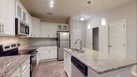 Located at 7108 Woods Walk in Villa Rica, Georgia, this single-story residence offers a well-designed layout with consistent, modern finishes throughout. The kitchen serves as a central highlight, featuring crisp white cabinetry with beadboard detailing, granite countertops, and a full suite of stainless steel appliances including a refrigerator, range, microwave, and dishwasher. A central island with a double stainless steel sink provides additional prep space and is complemented by pendant lighting overhead. A tasteful tile backsplash adds texture behind the range, while wood-look flooring runs throughout the space, providing a warm, cohesive aesthetic.

The living areas are bright and open, with neutral gray walls, white baseboards, and ceiling fans in each room. Natural light enters through multiple windows fitted with horizontal blinds, contributing to an airy atmosphere. A walk-in closet is visible off the main hallway, offering practical storage.

The bathrooms are finished with the same granite vanity tops and white cabinetry seen in the kitchen. One bathroom features a large walk-in shower with sliding glass doors and brushed nickel hardware, while another includes dual windows that bring in natural light. Wood-look flooring carries through both bathrooms, maintaining a unified design throughout the home.