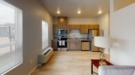 Located at 1408 21st Ave NW in Austin, Minnesota, this single-floor unit offers a thoughtfully designed layout that maximizes functionality and comfort. The open-concept living and kitchen area serves as the heart of the space, featuring light wood-style flooring that extends throughout and recessed lighting overhead. The kitchen is well-equipped with stainless steel appliances, including a refrigerator, electric range with microwave above, and dishwasher. Warm-toned wood cabinetry provides ample storage, while granite-style countertops and a double basin sink add a refined touch. A wall-mounted HVAC unit ensures year-round climate control, and a window allows natural light into the living area. The bedroom offers a cozy, private retreat with a distinctively painted ceiling accent and ample wall space. The full bathroom is finished with a granite-topped vanity, wood cabinetry with brushed nickel hardware, a framed mirror, and a tub-shower combination. A utility hallway provides access to the electrical panel and additional rooms via a stylish sliding barn door. The unit's clean, neutral palette and modern finishes create a cohesive and welcoming atmosphere throughout.
