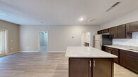 This single-story unit offers a thoughtfully designed open-concept layout that maximizes its footprint across one floor. The combined kitchen and living area forms the heart of the space, where the kitchen stands out with rich dark-espresso cabinetry, light granite countertops, a white subway tile backsplash, and a full suite of stainless steel appliances including a refrigerator, range, microwave, and dishwasher. A central island with matching granite provides additional prep and dining space. Light wood-style flooring runs consistently throughout the main living areas, creating a cohesive, clean aesthetic.

The living area is open and airy, with neutral warm-toned walls and a ceiling fan. Glass panel doors invite natural light and provide outdoor access. The bedroom is a comfortable size, featuring a window with blinds, a ceiling vent, and direct access to both a dedicated closet fitted with full-width wire shelving and the full bathroom. The bathroom includes large-format tile flooring, a granite-topped vanity with dark cabinetry, a mirror, and a tub-shower combination. The overall design is modern and neutral, offering a move-in-ready environment with consistent finishes throughout.