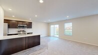 Located at 14703 Gul St. in the Copper Creek Villas community of Huntertown, Indiana, this two-story home offers a thoughtfully designed layout with clean, contemporary finishes throughout. The main level centers on an open-concept living and kitchen area, where light-toned walls and recessed lighting create a bright, welcoming atmosphere. The kitchen is well-appointed with dark espresso cabinetry, light countertops, stainless steel appliances including a refrigerator, range, microwave, and dishwasher, and a central island with a sink that overlooks the living space. Light wood-look flooring runs through the kitchen and transitions to plush neutral carpeting in the living area. A sliding glass door and an adjacent window allow natural light to flow in while providing direct access to the outdoors. Additional rooms on the upper level feature soft carpeting, neutral walls, and recessed lighting, offering versatile living spaces. A full bathroom includes a tub-shower combination with brushed nickel fixtures and clean white surrounds. The overall design presents a move-in-ready home with a cohesive, modern aesthetic suited for comfortable everyday living.