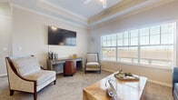 Located in Krum, Texas, this thoughtfully designed one-bedroom, one-bathroom residence offers a comfortable and functional layout across a single floor. The living area immediately impresses with its elegant tray ceiling accented by crown molding, plush carpeting, and large windows fitted with blinds that allow abundant natural light while maintaining privacy. The open-concept kitchen and dining area is efficiently arranged, featuring dark espresso cabinetry with modern hardware, a light-toned tile backsplash, wood-look flooring, and full appliances including a range and refrigerator. The adjacent dining space is defined by a warm, neutral color palette and chair-rail molding, creating a refined yet inviting atmosphere. The bedroom is generously sized with soft carpet, dual windows overlooking the outdoors, and direct access to a walk-in closet with built-in shelving. The full bathroom exudes a clean, modern feel with dark wood vanity cabinetry, a dual-sink countertop, a large mirror with Hollywood-style lighting, and tile flooring in a wood-plank pattern. A dedicated laundry area and a carpeted staircase with a wood handrail round out the practical amenities of this well-finished residence.
