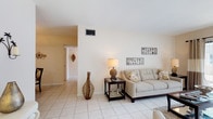 This single-floor residence offers a thoughtfully designed layout that balances comfort and functionality throughout. The living room serves as the heart of the home, featuring light-toned tile flooring, neutral walls, and a sliding glass door that fills the space with natural light and provides access to an outdoor area. The room comfortably accommodates a seating arrangement and offers a welcoming, open ambiance.

Adjacent to the living area, the dining space is defined by tile flooring and a pendant light fixture overhead, creating an intimate setting ideal for everyday meals or entertaining. The galley-style kitchen is efficiently organized with light wood cabinetry lining both sides, granite-style countertops, a stainless steel sink, and tile flooring, maximizing storage and workspace.

The residence includes multiple bedrooms, each carpeted for warmth and comfort. The primary bedroom is generously proportioned with a large window allowing ample natural light, and benefits from access to a spacious walk-in closet outfitted with extensive wire shelving and hanging systems. Additional bedrooms offer closet access and window views. The bathroom is finished with tile flooring, wood cabinetry with a stone-topped vanity, a large mirror, and a glass-enclosed walk-in shower, providing a clean and practical design throughout.