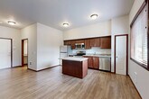 Located at 140 S Olympic Ave in Arlington, Washington, this thoughtfully designed unit offers a practical and modern layout across a single floor. The open-concept kitchen and living area serves as the heart of the space, anchored by a central island with a granite countertop that provides additional prep space and casual seating. Rich, dark-wood cabinetry lines the kitchen walls, complemented by stainless steel appliances including a refrigerator, range, microwave, and dishwasher. Light wood-look flooring flows seamlessly throughout, brightening the interior and creating a cohesive feel. A window in the living area invites natural light and offers views of the surrounding greenery. A stylish sliding barn door adds a contemporary architectural touch, leading into the den — a flexible space ideal for a home office or additional sleeping area. The bathroom is well-appointed with a granite-topped vanity, rich wood cabinetry, and the added convenience of a stacked in-unit washer and dryer. Dark wood trim accents throughout the unit provide a polished contrast to the neutral white walls. A dedicated closet offers practical storage solutions. The overall ambiance is clean, modern, and efficient, making excellent use of every square foot.