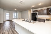 This single-story unit is designed with a practical, open-concept layout that connects the kitchen and living areas seamlessly. The kitchen is a functional centerpiece, equipped with dark cabinetry, light countertops, a large peninsula with a double stainless steel sink, black appliances including a refrigerator, electric range, and microwave, and recessed lighting overhead. Wood-look hard flooring extends throughout the main living spaces, adding warmth and durability.

The living area is generously proportioned and filled with natural light from a window overlooking the surrounding neighborhood. A dedicated closet in this area houses a stacked washer and dryer unit, providing in-unit laundry convenience. An exterior door offers additional access from the living space.

The bedrooms feature plush carpeting, ceiling fans with light fixtures, and large windows that bring in natural light and neighborhood views. Two bathrooms serve the unit: one features a full tub/shower combination with clean white finishes and light wood-look flooring, while the other includes a vanity with dark cabinetry and direct access to a walk-in closet with built-in shelving. The overall aesthetic is clean, modern, and neutral throughout.