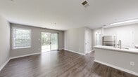 Located at 7109 Rock Ridge Ln in Alexandria, VA, this single-floor residence offers a clean, modern aesthetic throughout. The open-concept living and dining area is finished with rich wood-tone luxury vinyl plank flooring and neutral gray walls, creating a bright, cohesive atmosphere. Sliding glass doors lead to a private balcony overlooking lush greenery, filling the space with natural light.

The kitchen is thoughtfully designed with white shaker-style upper cabinets, gray lower cabinets, white quartz countertops, a subway tile backsplash, and stainless steel appliances including a refrigerator, range, microwave, and dishwasher. A peninsula with an undermount sink opens toward the main living area.

The bedrooms offer plush carpeting and large windows with slatted blinds that frame tree-lined outdoor views. One bedroom features a double-door closet, while another connects directly to a full bathroom. A hallway bathroom includes a tub-shower combination with clean white surrounds. Throughout the home, white panel doors, brushed nickel hardware, and consistent trim details contribute to a polished, well-maintained finish. This residence combines practical functionality with modern design in a serene Alexandria setting.