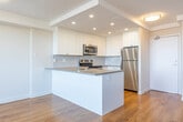 Located at 108 Edgehill Dr in Barrie, Ontario, this 2-bedroom, 1-bathroom unit offers a well-designed layout with consistent warm hardwood-style flooring throughout. The open-concept living and kitchen area forms the heart of the unit, where large windows and a sliding glass door flood the space with natural light while offering elevated views of the surrounding cityscape and treeline. The kitchen is outfitted with white shaker-style cabinetry, light stone countertops, a peninsula with a stainless steel sink, and a full suite of stainless steel appliances including a range, built-in microwave, and dishwasher, complemented by recessed lighting overhead. The living area is spacious and bright, with a textured ceiling and ample room for comfortable furnishings. Both bedrooms are finished with the same hardwood-style flooring and bright white walls; the primary bedroom features a closet and a large window with outdoor views, while the second bedroom also benefits from natural light. The bathroom includes a vanity with stone countertop, mirrored medicine cabinet, and a full bathtub with shower. A dedicated utility closet houses the water heater, and in-unit laundry facilities are also included, adding everyday convenience to this clean and functional Barrie residence.