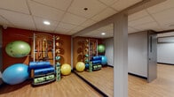 Located at 1188 Main St in Bridgeport, Connecticut, this single-floor fitness facility is thoughtfully organized into multiple distinct workout zones, each designed to support a variety of training styles. Throughout the space, light hardwood flooring, drop tile ceilings with recessed lighting, and a warm two-tone color scheme of burnt orange and slate gray create a focused yet welcoming athletic environment.

The free weights area is equipped with a full rack of dumbbells ranging across multiple weight increments, paired with an adjustable bench and floor-to-ceiling mirrors that enhance spatial depth and allow for form monitoring during workouts. A dedicated strength training zone houses a power rack with a barbell and weight plates alongside a standalone plate-loaded station, ideal for compound and isolation lifts.

A separate functional training room features an array of stability balls, resistance bands, medicine balls, and foam rollers organized on wall-mounted racks, with large mirrors and warm-toned walls contributing to an energetic atmosphere. An additional room accommodates a multi-function cable machine for targeted resistance exercises.

The facility also includes a transitional corridor area with built-in storage cubbies and coat hooks, offering a practical space for personal belongings. The overall layout provides ample room to move freely between training stations, making this a well-rounded fitness space suited for diverse exercise programs.