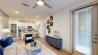 This single-story residence combines modern design with functional living across a thoughtfully arranged open-concept floor plan. Light wood-tone flooring runs throughout the main living areas, complementing crisp white walls and recessed lighting that keep the space feeling bright and airy. Ceiling fans in both the living room and bedrooms add a practical touch while reinforcing the clean, contemporary aesthetic.

The living area offers generous room for seating and entertaining, with multiple windows fitted with blinds that allow for controlled natural light. A sliding glass door provides access to an outdoor area, further enhancing the sense of openness. The kitchen is a standout feature, equipped with white shaker-style cabinetry, granite-look countertops, stainless steel appliances including a side-by-side refrigerator, electric range, and built-in microwave, as well as a subway tile backsplash. A peninsula island with bar seating and an adjacent open pantry add notable storage and functionality.

The primary bedroom features a soothing blue-grey accent wall, plush carpet, and ample natural light from well-positioned windows. The secondary bedroom mirrors the calm atmosphere with neutral tones and natural light. The bathroom presents white cabinetry, a granite-topped vanity, and a framed mirror, maintaining the cohesive, polished style found throughout the residence.