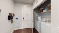 This well-appointed single-floor residence offers a thoughtfully designed open-concept layout with contemporary finishes throughout. The kitchen serves as the heart of the home, showcasing a large granite-topped island with bar seating, pendant lighting, stainless steel appliances, a subway tile backsplash, and a two-tone cabinet scheme combining crisp white uppers with warm wood-toned lowers. Rich, dark hardwood flooring runs continuously through the main living areas, adding warmth and cohesion.

The living room is bright and welcoming, with multiple large windows dressed in linen drapes that allow generous natural light and outdoor views. Adjacent to it, a dedicated dining area features a glass-panel door leading to a balcony, enhancing the sense of openness. Both bedrooms are carpeted for comfort and include ceiling fans, large windows, and ample natural light. The full bathroom is elegantly finished with a granite double vanity, glass-enclosed shower-tub combination, and recessed lighting.

Completing the unit is a functional laundry area near the entry, equipped with a full-size washer and dryer and overhead built-in shelving for added storage. A smart home thermostat and keypad entry at the front door reflect the residence's modern, convenience-focused design.