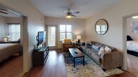 This single-floor residence offers a thoughtfully designed layout that balances comfort and functionality across multiple rooms. The living area serves as the heart of the home, featuring rich hardwood flooring, a ceiling fan, and multiple windows with slatted blinds that invite abundant natural light. The open flow connects seamlessly to the kitchen, which is equipped with dark espresso cabinetry, granite countertops, stainless steel appliances including a refrigerator and microwave, a gas range, and track lighting overhead. A dedicated laundry area is conveniently accessible from the kitchen. Each bedroom is carpeted for warmth and comfort, fitted with ceiling fans, and offers generous natural light through well-positioned windows. The primary bedroom includes access to a walk-in closet and an en-suite bathroom featuring hardwood flooring, a granite-topped vanity with dark cabinetry, and a shower. A second bathroom mirrors this design with similar finishes, providing a consistent aesthetic throughout. The neutral warm tones on the walls create a welcoming ambiance, while the consistent use of dark espresso wood finishes across cabinetry and furniture ties the overall design together cohesively.