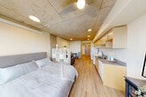 Located at 1400 Madison Street in Seattle's First Hill neighborhood, this efficiently designed studio unit offers a thoughtful layout across a single floor. The entrance corridor, lined with light hardwood flooring and recessed lighting, leads directly into the combined kitchen and living area that forms the heart of the space.

The kitchen is well-appointed with light maple cabinetry extending to the ceiling, a full-size refrigerator, an electric range and oven, a double-basin sink with ample counter space, and a built-in dishwasher. The exposed concrete ceiling overhead lends an industrial character that contrasts warmly with the natural wood tones of the cabinetry and flooring throughout.

The open living and sleeping area is bright and airy, benefiting from large windows that invite natural light and frame views of the surrounding Seattle skyline. A freestanding shelving unit provides a functional visual partition between the sleeping and lounge zones, allowing for a defined sense of separation within the open plan. A ceiling fan adds to the comfort of the space.

The bathroom is clean and functional, featuring a shower-tub combination with a curtain enclosure, a toilet, and a vanity. A dedicated closet near the entrance provides convenient storage. The overall ambiance is modern and understated, with a neutral palette that feels calm and livable.