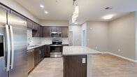 Located at Rolling Hills Circle in Easley, SC, this single-story, one-bedroom, one-bathroom unit offers a thoughtfully designed layout that maximizes functionality. The open-concept kitchen and living area serves as the heart of the space, featuring light wood-tone flooring, dark espresso cabinetry, granite countertops, and a full suite of stainless steel appliances including a refrigerator, range, microwave, and dishwasher. A central kitchen island with pendant lighting above provides additional prep and seating space, while built-in shelving near the entryway adds convenient storage. A glass-panel door and adjacent window in the living area invite abundant natural light and outdoor views. The bedroom is carpeted and includes a ceiling fan and a window overlooking the outdoors. The bathroom features a granite-topped vanity with dark cabinetry, a tiled tub-shower combination, and wood-look flooring. A dedicated laundry room with hookups and a separate closet round out the unit. Neutral warm-toned walls throughout create a cohesive, welcoming ambiance.